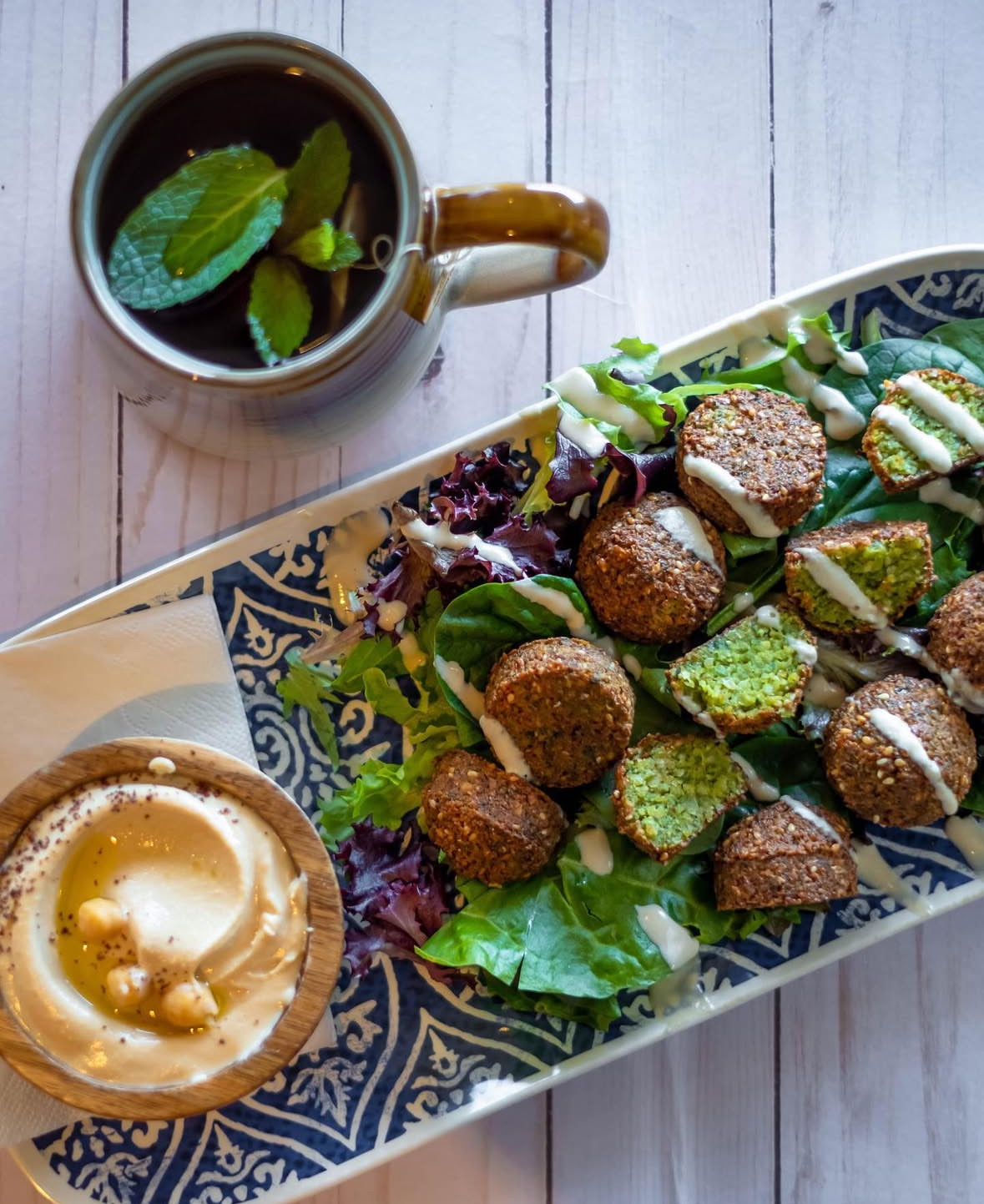 Fresh falafel with deep green herb interior, golden crust, tahini drizzle and hummus — Yafa Hummus